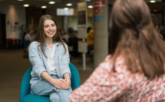 Student sat smiling at colleague with hands crossed on knee